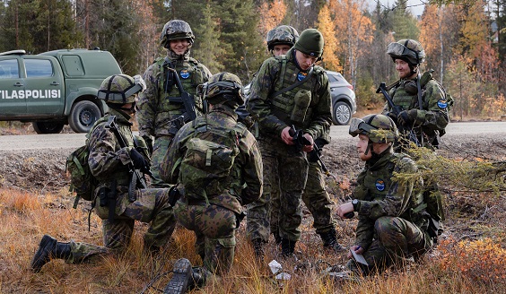 Kuvassa seitsemän reserviläistä taisteluvarustuksessa Ruska 22 -harjoituksessa. Taustalla sotilaspoliisiauto..