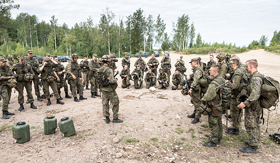 Maastopukuisia sotilaita ringissä, yksi, eli johtaja, on keskellä.