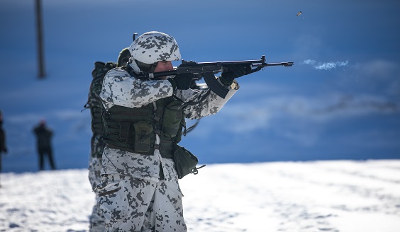 Lumipukuinen sotilas tähtää rynnäkökiväärillä ja ampuu.