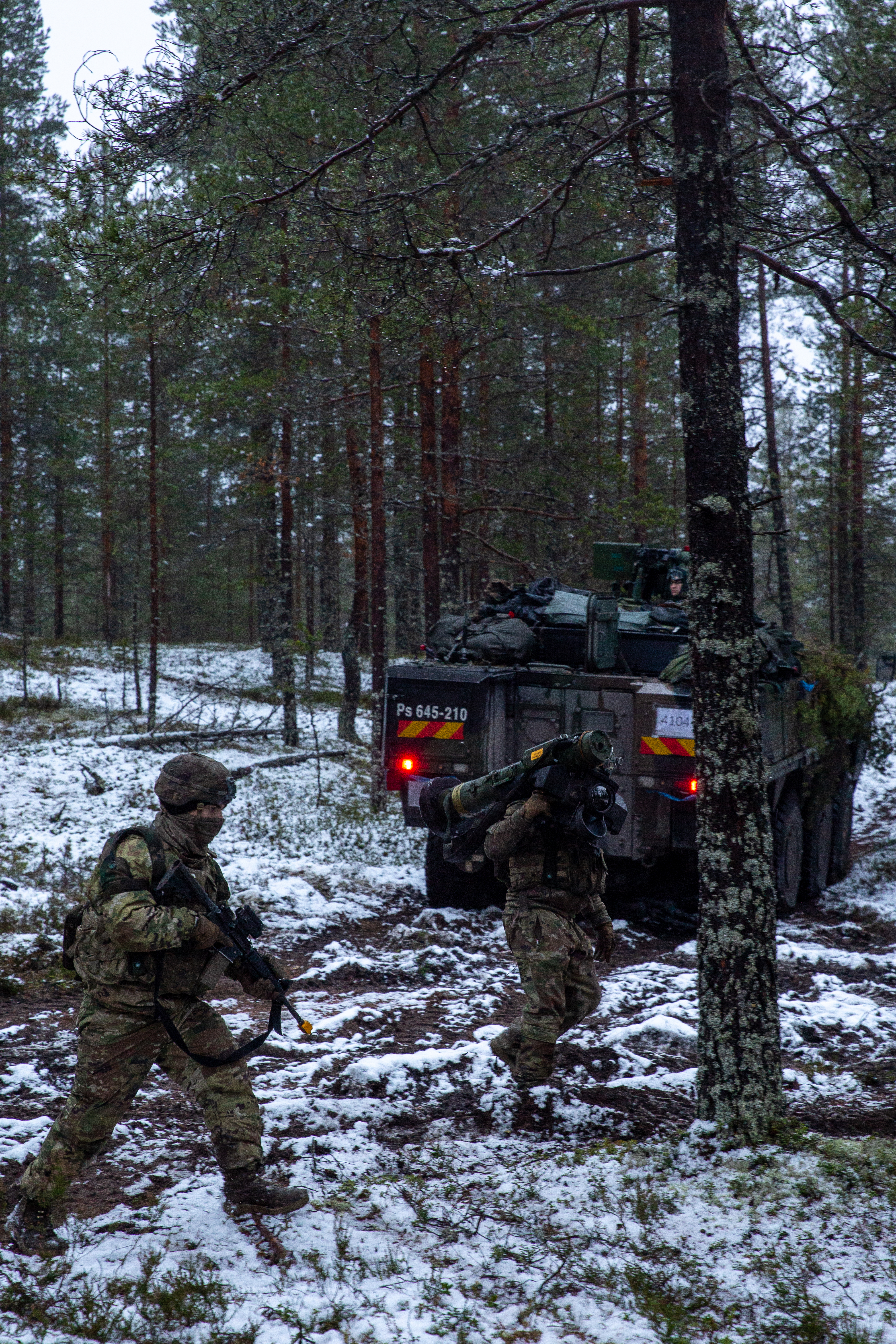 Kaksi yhdysvaltalaista sotilasta kävelee talvisessa metsässä, taustalla suomalaisten panssarivaunu.