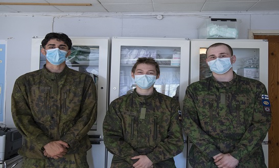 Kolme varusmiestä maastopuvuissa poseeraa lääkekaapin edessä.