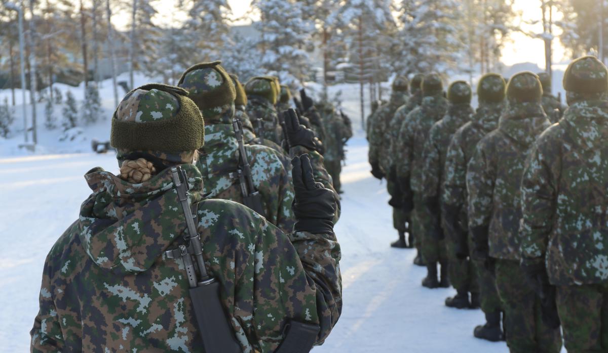 Sotilaita talvisessa maisemassa oikean käden kaksi sormea pystyyn nostettuina.