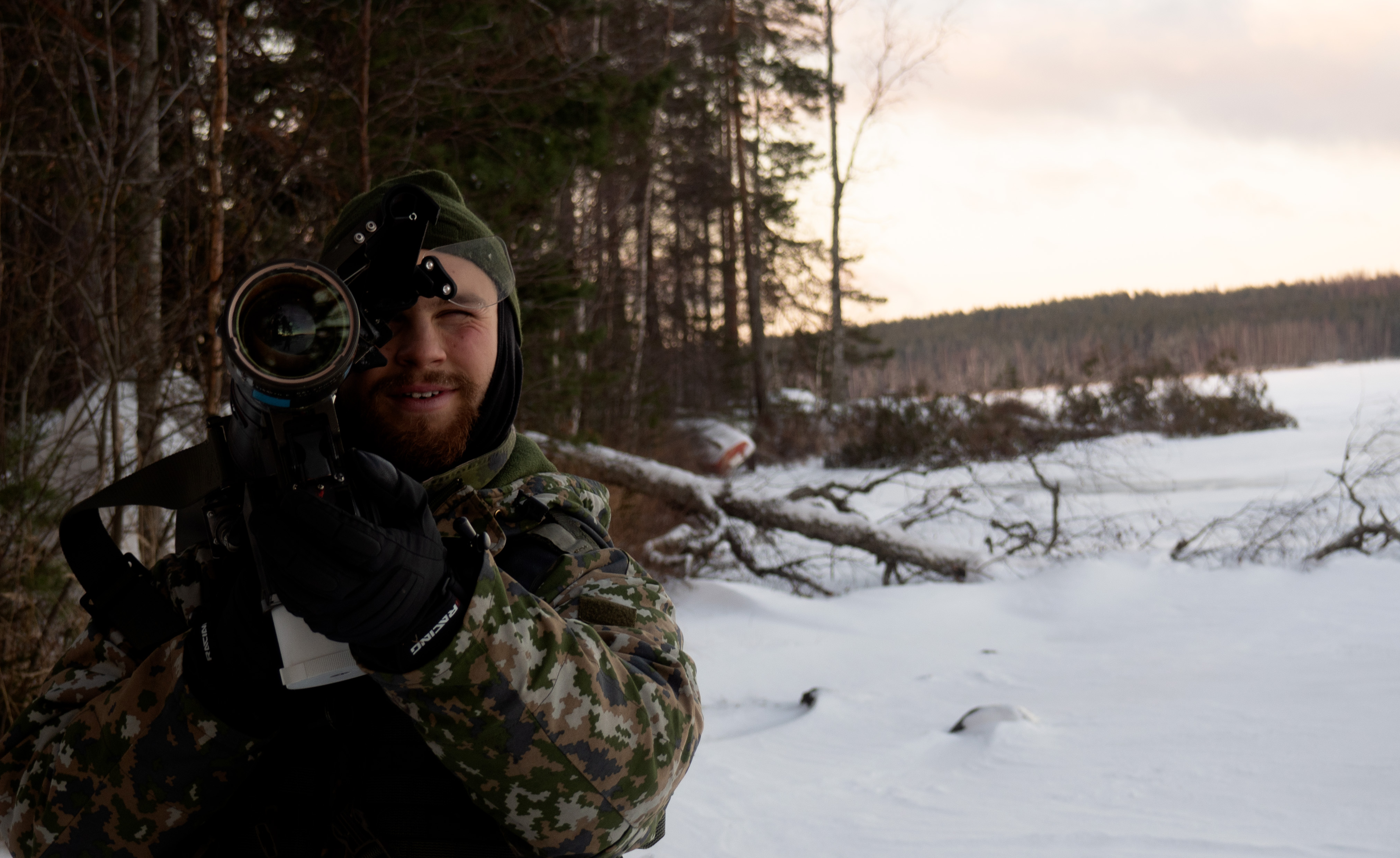 sotilas talvisen järven rannalla, osoittaa ilmatorjuntaohjuksella kohti kameraa.