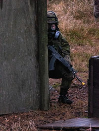 sotilas tarkkailee suojanaamari päässä rynnäkkökiväärin kanssa kulman takana