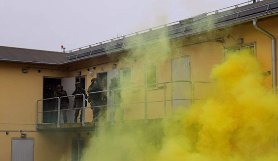 Sotilaat juoksevat toisen kerroksen parvekkeella aseilla tähdäten keltaisen savun suojassa