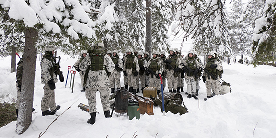 Sotilaat muodossa lumisessa metsässä. Maassa on leiriytymiskalustoa.