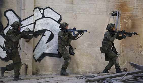 Kolme sotilasta juoksee aseiden kanssa vanhassa rakennuksessa.