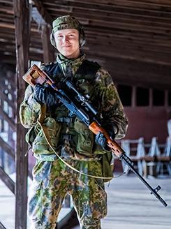 varusmies, jolla on päässä kuulosuojaimet, pitelee käsissään asett. Taustalla ampumarataa.