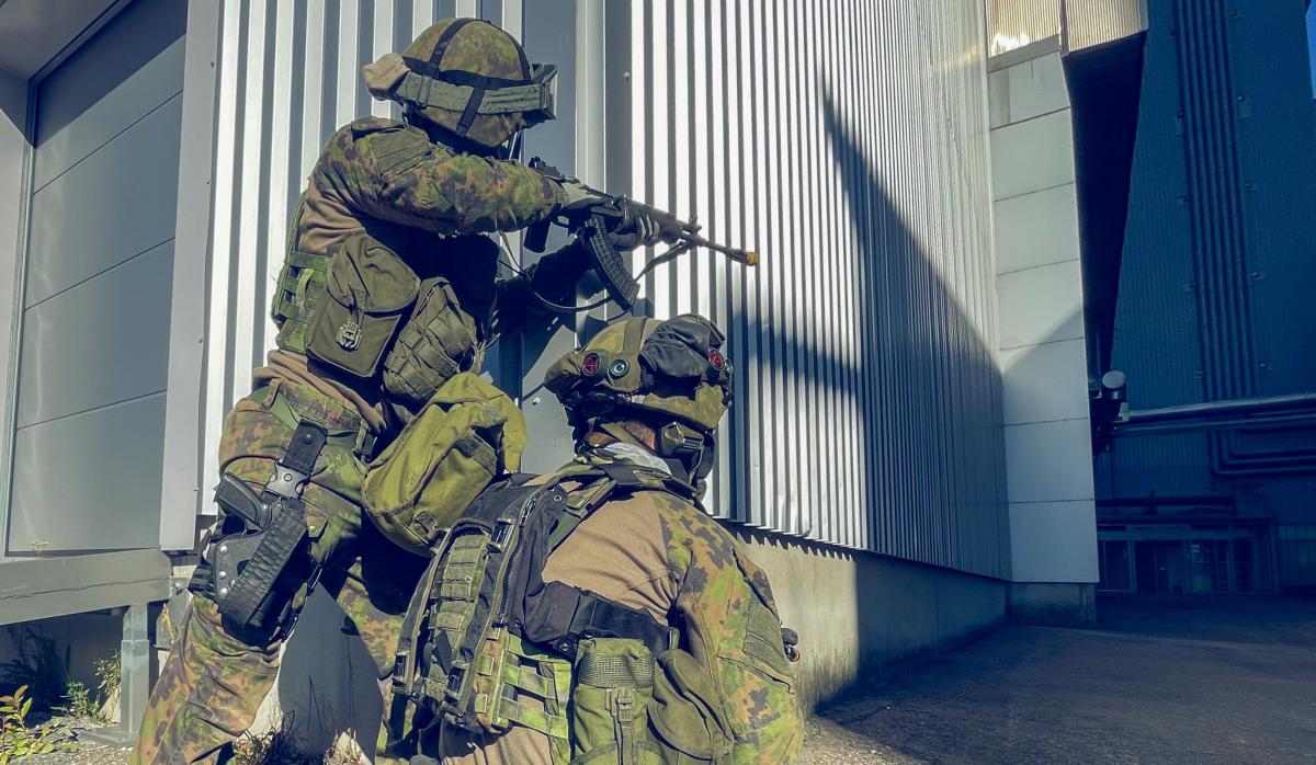 Kuvassa kaksi taisteluvarustuksessa olevaa sotilaspoliisia etenemisvalmiudessa rakennuksen nurkalla.