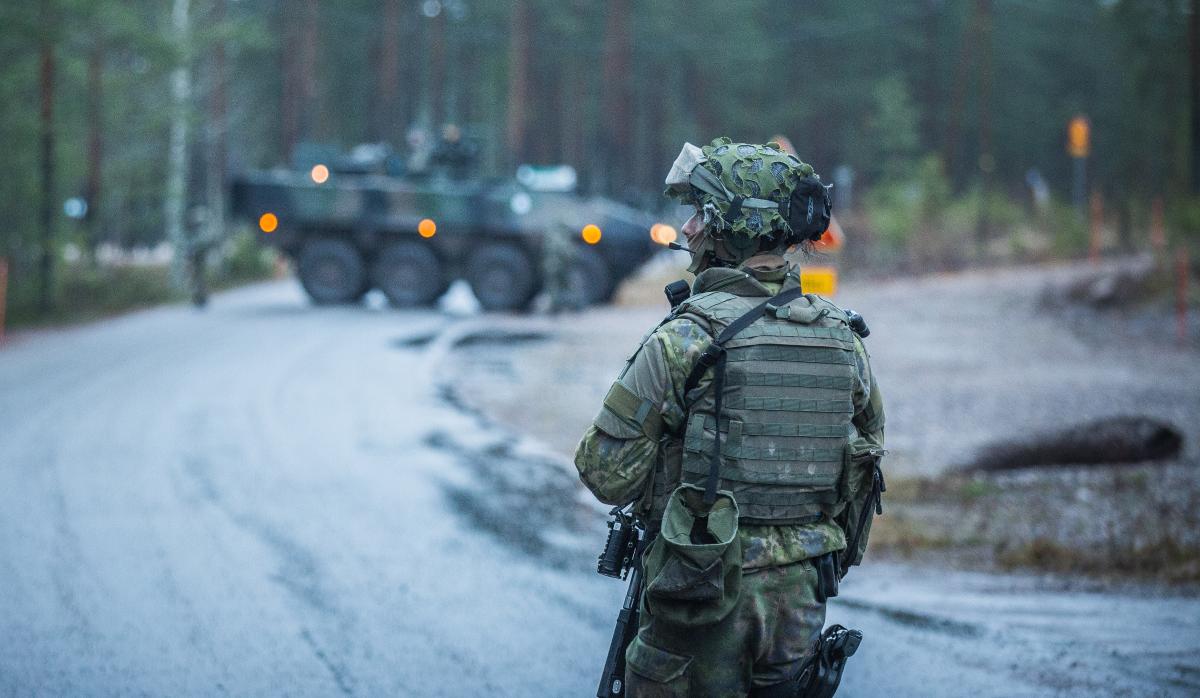 Kuvassa etualalla seisoo Suomen kansainvälisen valmiusjoukon varusmies taisteluvarustuksessa ja takana näkyy kuljetuspanssariajoneuvo.