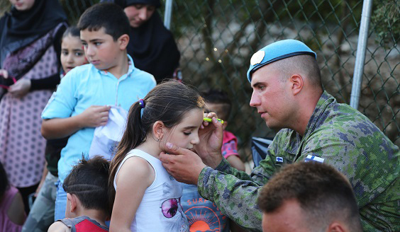 Sotilas piirtää kynällä lapsen otsaan