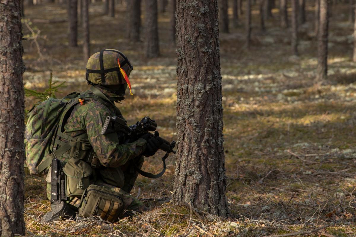 Kuvassa taisteluvarustuksessa oleva paikallisjoukkojen reserviläinen hakemassa suojaa puun takaa.