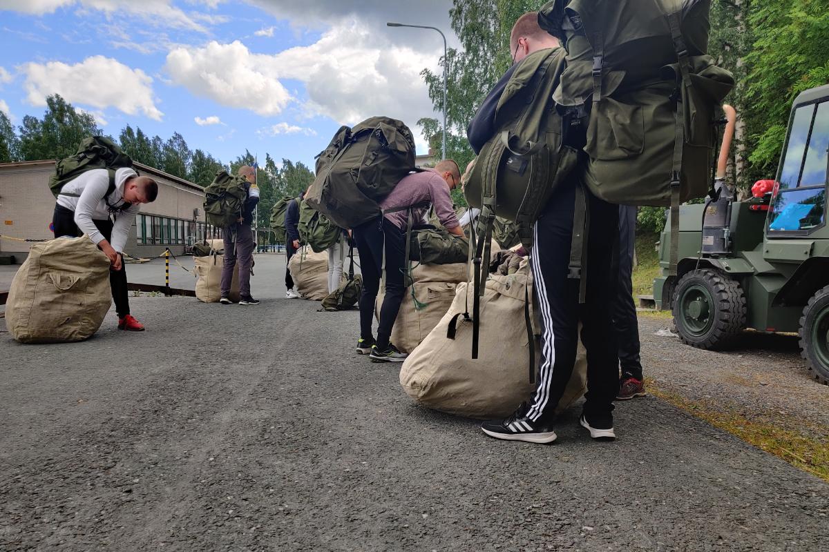 Varusmiespalveluksensa aloittaneet alokkaat pakkaavat saamiaan varustesäkkejä varuskunta-alueella kesäisessä säässä.