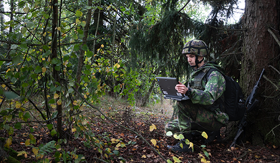 En soldat under ett träd med en bärbar dator i handen
