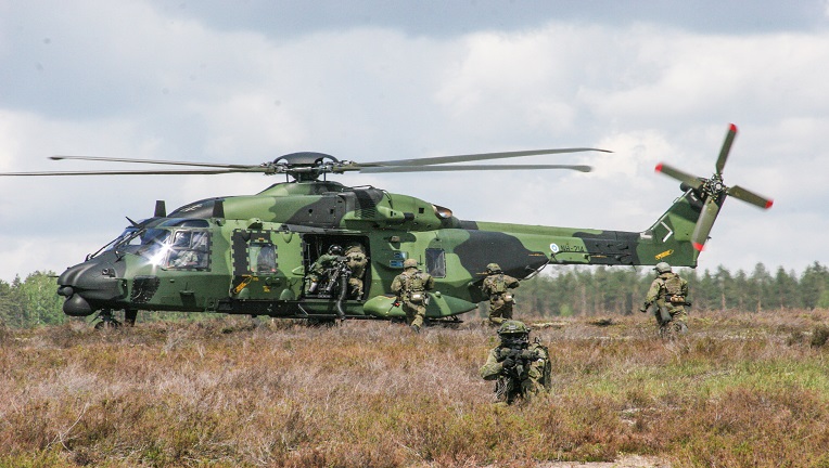 NH90-helikopteri laskeutuneena niitylle. Etualalla näkyy sotilaita.